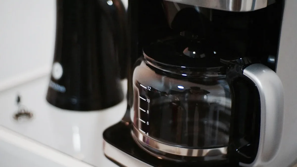 A coffee maker with a glass carafe and a black kettle on a white countertop.