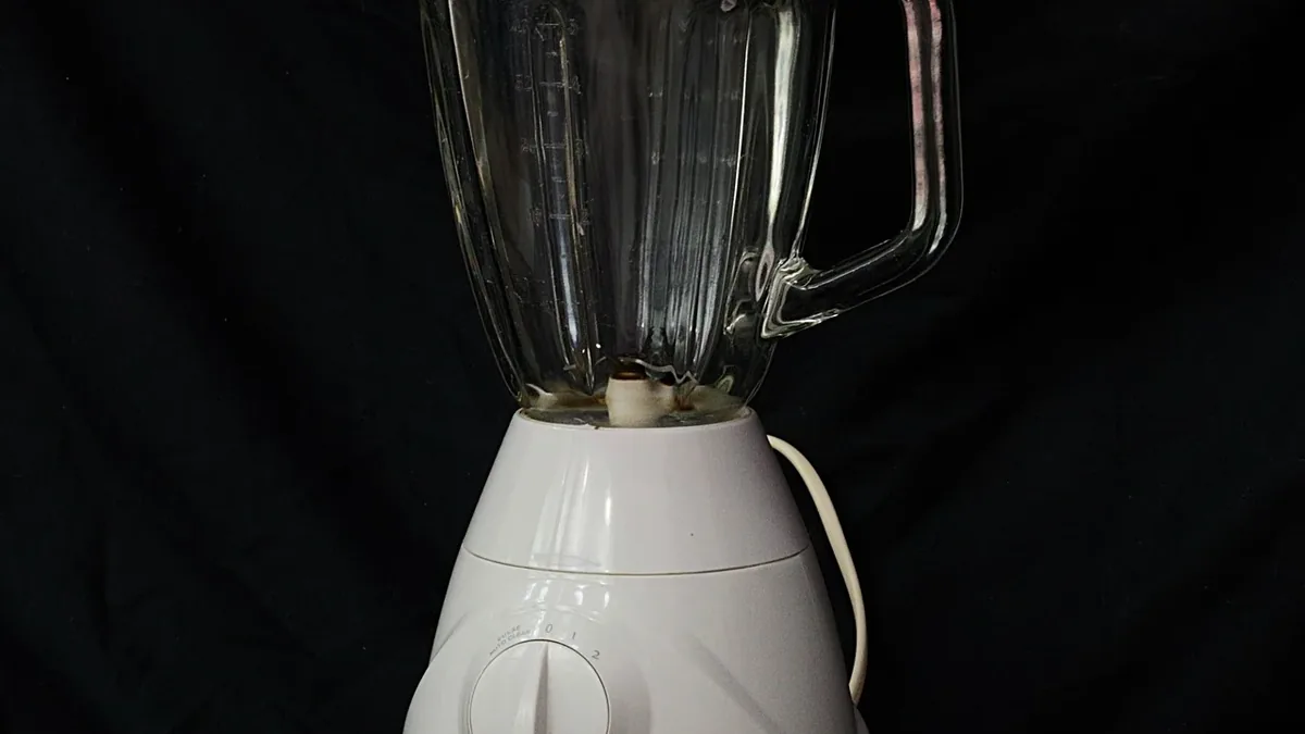 A white blender with a clear plastic pitcher and a handle on the right side.