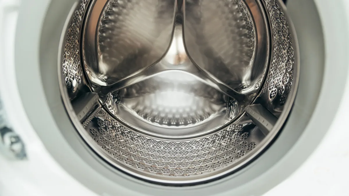 The interior of a washing machine drum, featuring a stainless steel bowl with a textured surface and a central agitator.